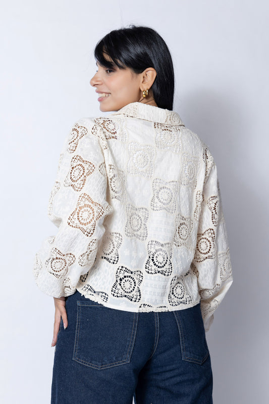 سيدة ترتدي بلوزة دانتيل بيضاء بتصميم مفرغ بأشكال زهرية، مع ياقة كلاسيكية وأكمام طويلة منفوخة، تقف بخفة وهي تبتسم وتنظر للأعلى في خلفية بيضاء.